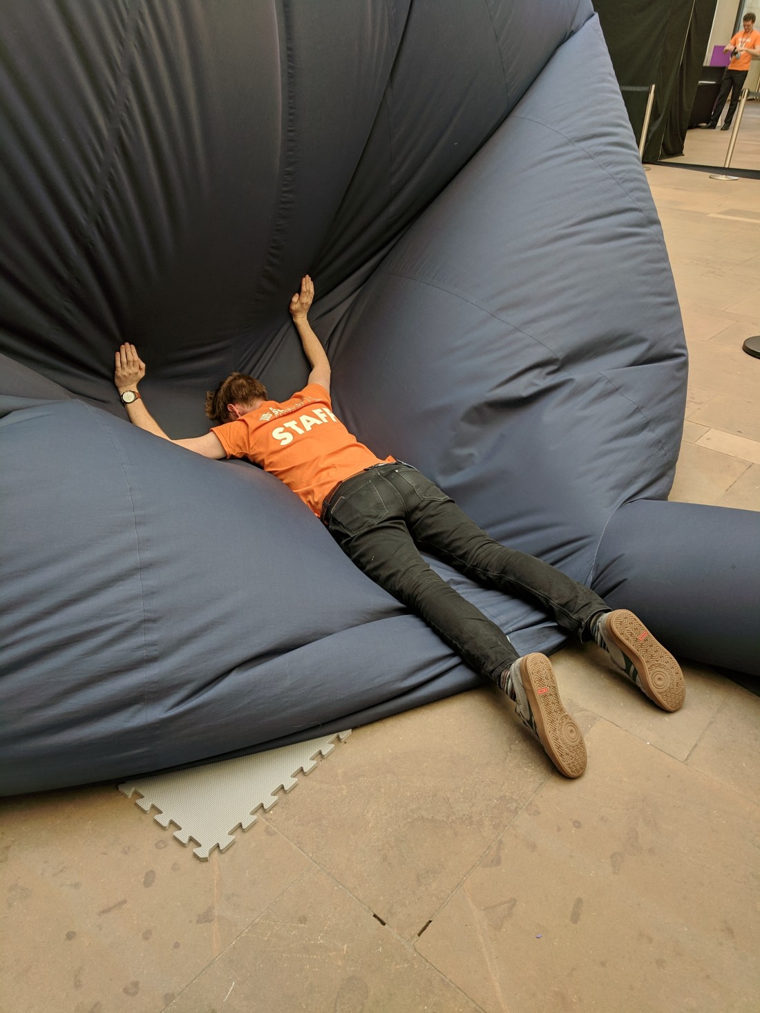 Man in orange shirt facedown flopping on blue cloth inflatable planetarium dome