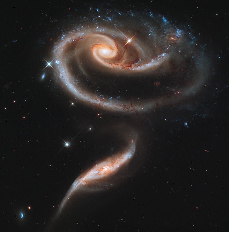 Large spiral galaxy floating next to smaller spiral galaxy in space.